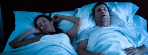 couple in bed, man snoring and woman covering ears