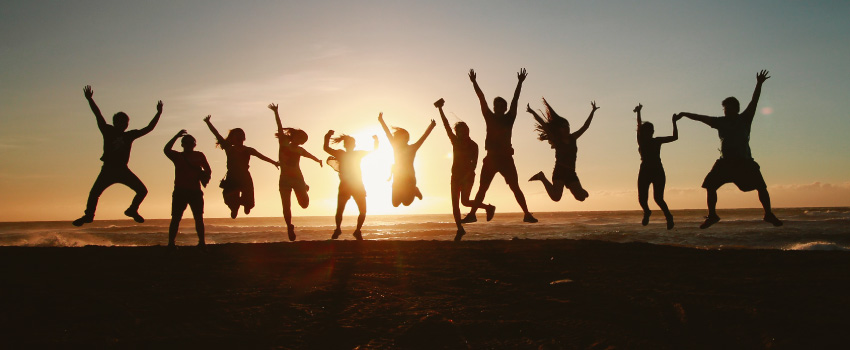 Silhouette of a group of people jumping up in excitement on a beach as the sun sets