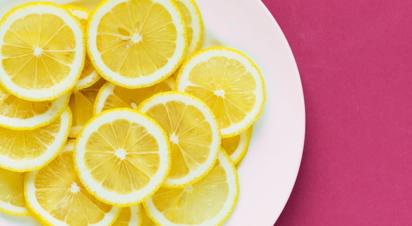 Aerial view of thinly sliced acidic lemons on a white plate on a pink counter