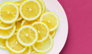 Aerial view of thinly sliced acidic lemons on a white plate on a pink counter