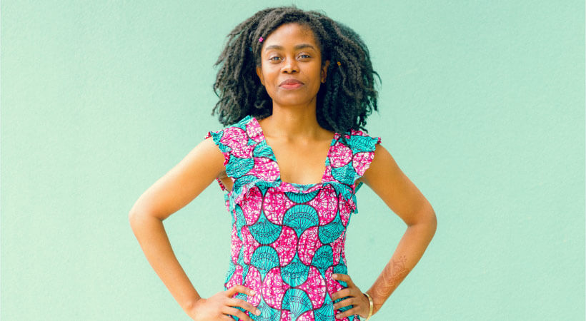 Dark-haired woman wearing a teal and hot pink floral dress stands in front of a mint wall thinking about electric toothbrushes