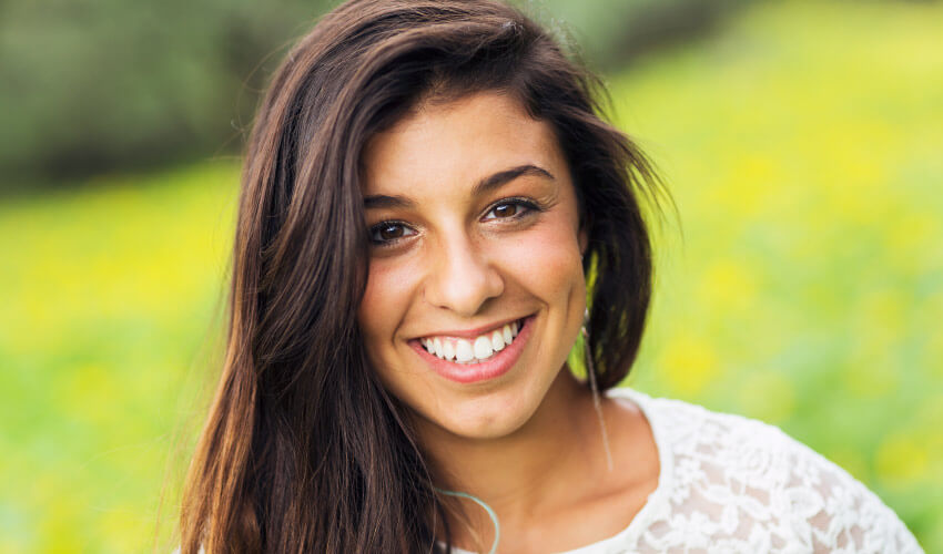 Closeup of a brunette young woman wearing a white shirt in a green meadow smiling with white teeth