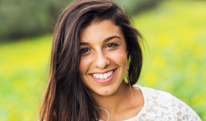 Closeup of brunette teenage girl in a green and yellow meadow smiling before her wisdom teeth removal at the dentist