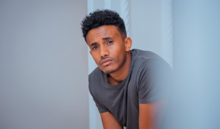 Dark-haired young man wearing a gray shirt sits by a white pillar feeling concerned about his daily oral hygiene mistakes