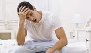 Brunette man in his pajamas yawns and has a morning headache and daytime sleepiness from sleep apnea