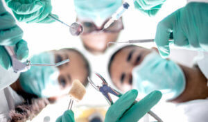 Looking up into 3 dentists in teal scrubs holding tools prepping for wisdom teeth removal