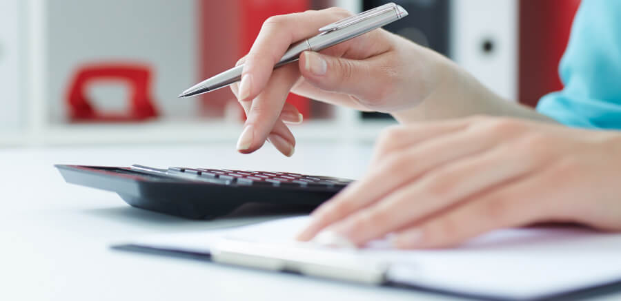 Hands shown adding up sums on a calculator with pen in hand