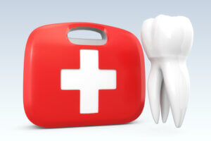 A red emergency kit with a white cross sitting next to a model of a tooth