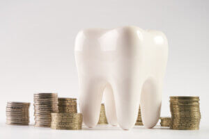A large model of a tooth sitting among stacks of coins.