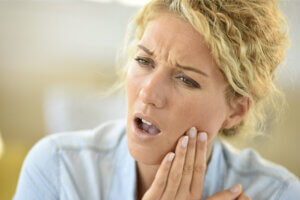 Blonde woman with her hand on her cheek indicating tooth pain.