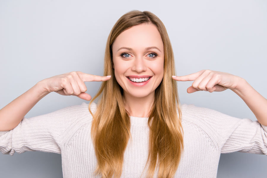 A smiling woman points at her white smile with both hands.